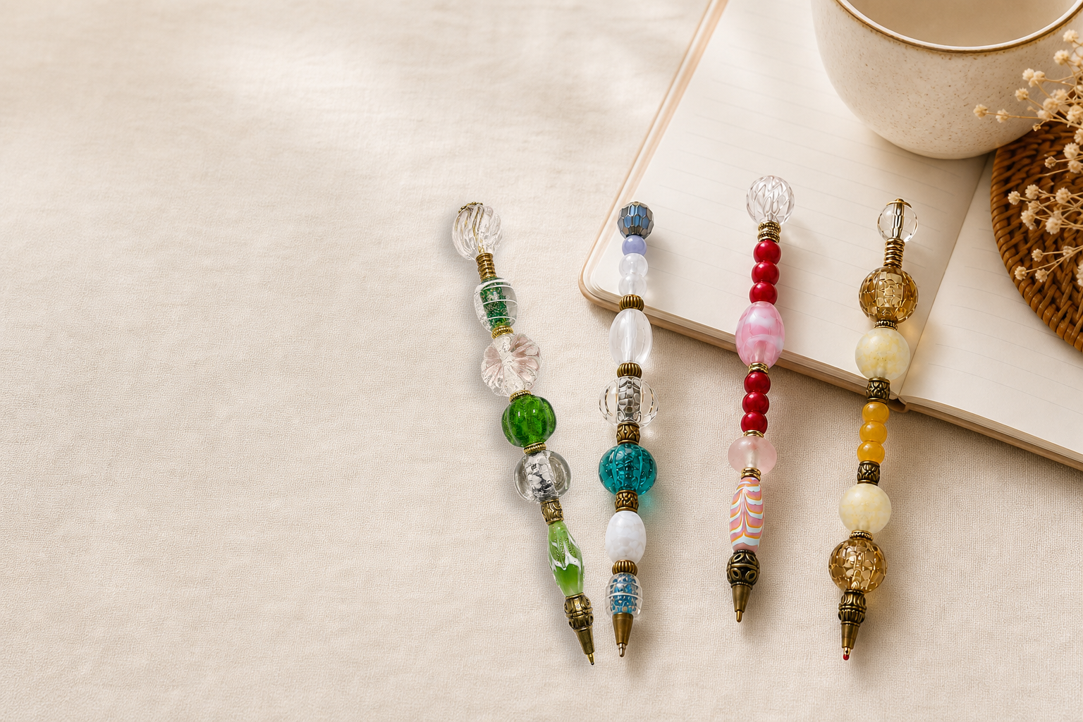 Four handmade beaded pens on a linen desk with notebook and coffee
